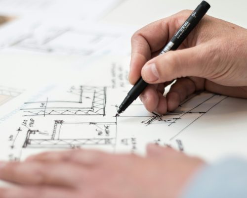 Close-up of hand drawing intricate technical designs on blueprint with pen, ideal for engineering or architecture themes.